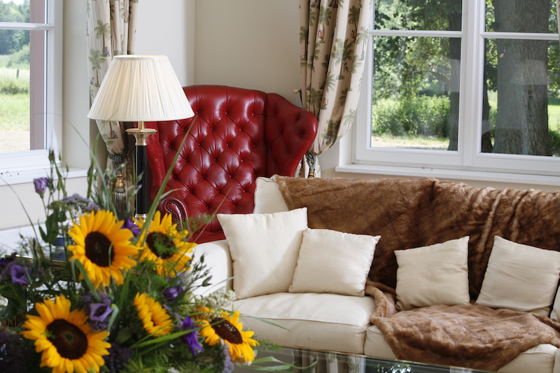 Sofa und roter Sessel in der Ecke des weißen Salons, im Vordergrund ein Blumenstrauß